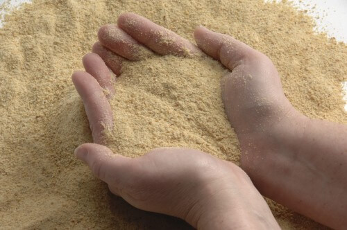 ExPress Soy Meal being held between to palms on top of more soymeal